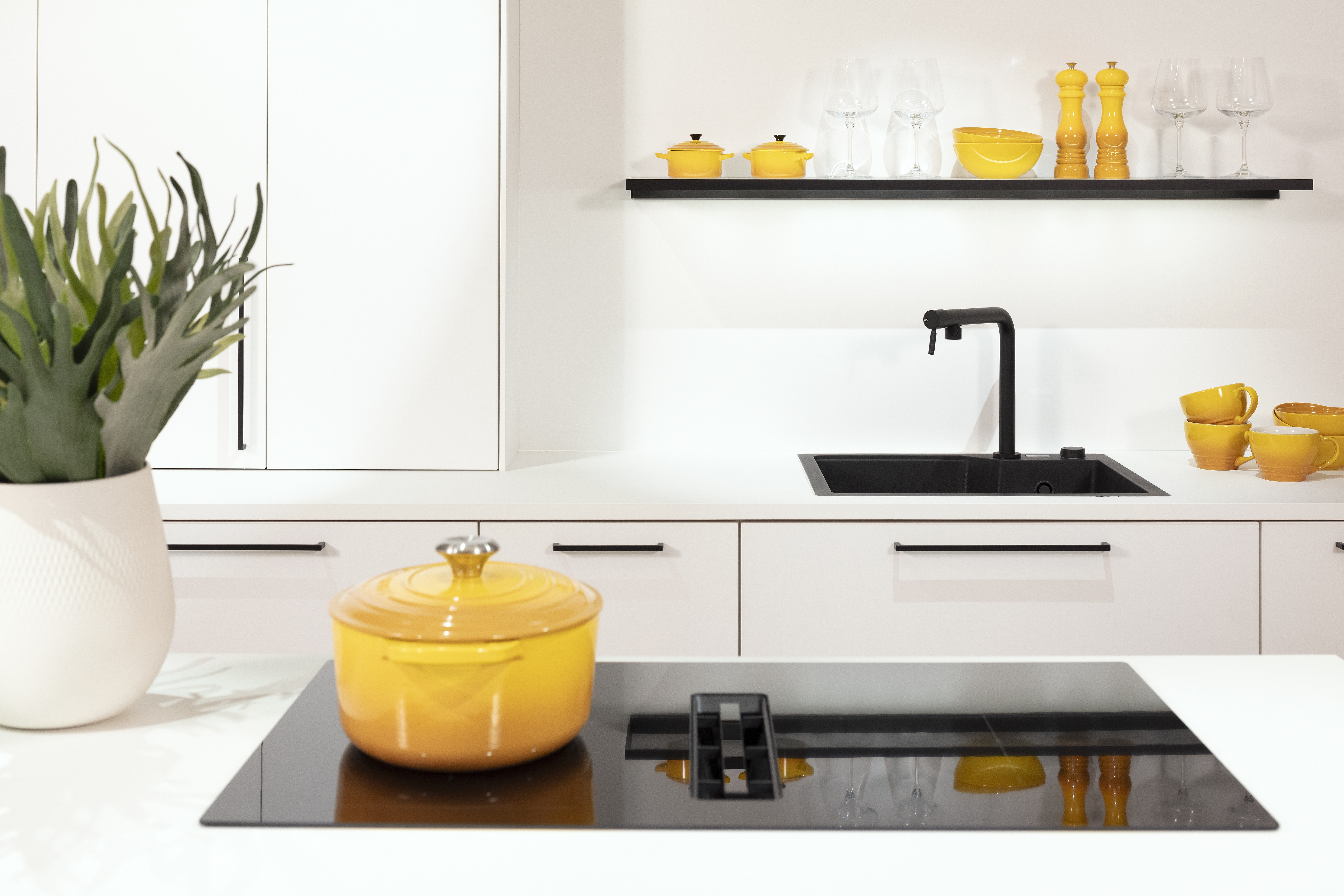 Kristallweiße Häcker-Küche mit Kochfeld auf Kücheninsel und Küchenzeile im Hintergrund