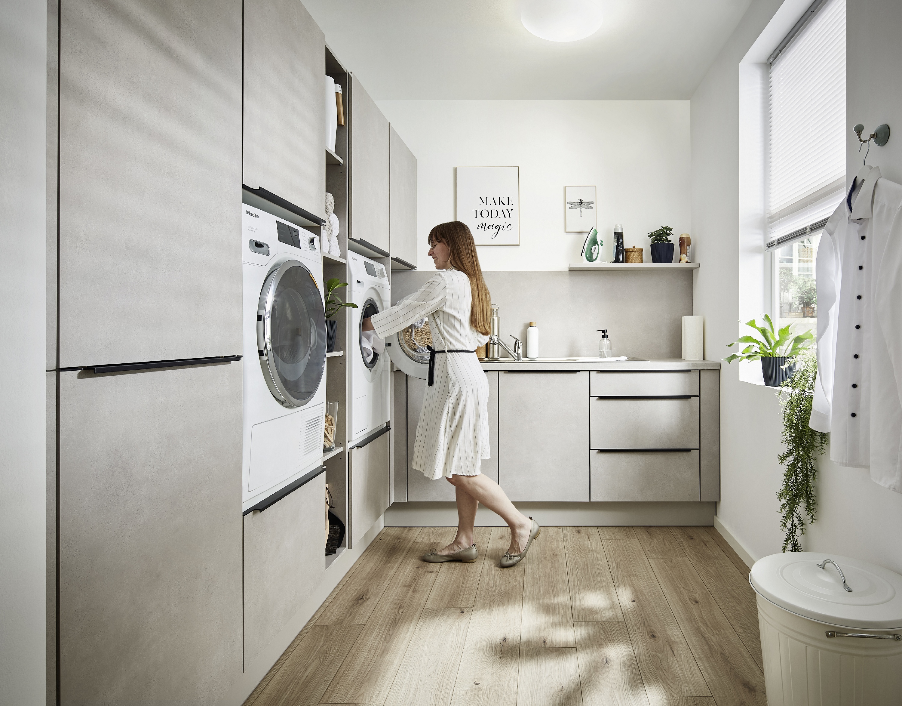 ergonomisch erhöht nebeneinander eingebaute Waschmaschine und Trockner Frau im Morgenmantel legt Wäsche in den Trockner