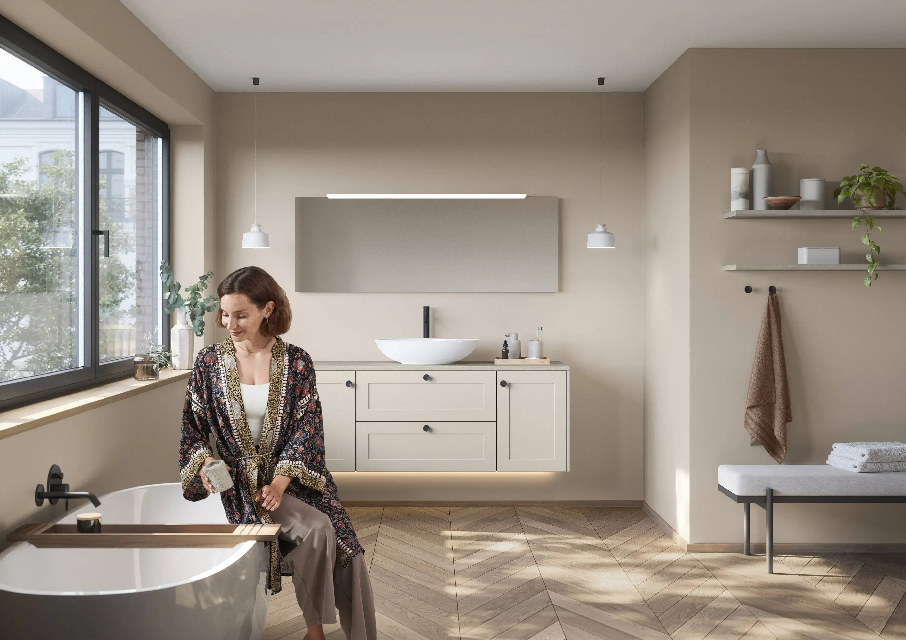 Badezimmer im modernen Landhausstil Fischgrätparkett weisse Waschschale auf cremeweissem Unterschrank mit Rahmenfronten und schwarzen Knaufgriffen Frau im feinen Morgenmantel sitzt lächelnd am Beckenrand ihrer freistehenden Badewanne und stellt Tiegel auf Wannenbrücke